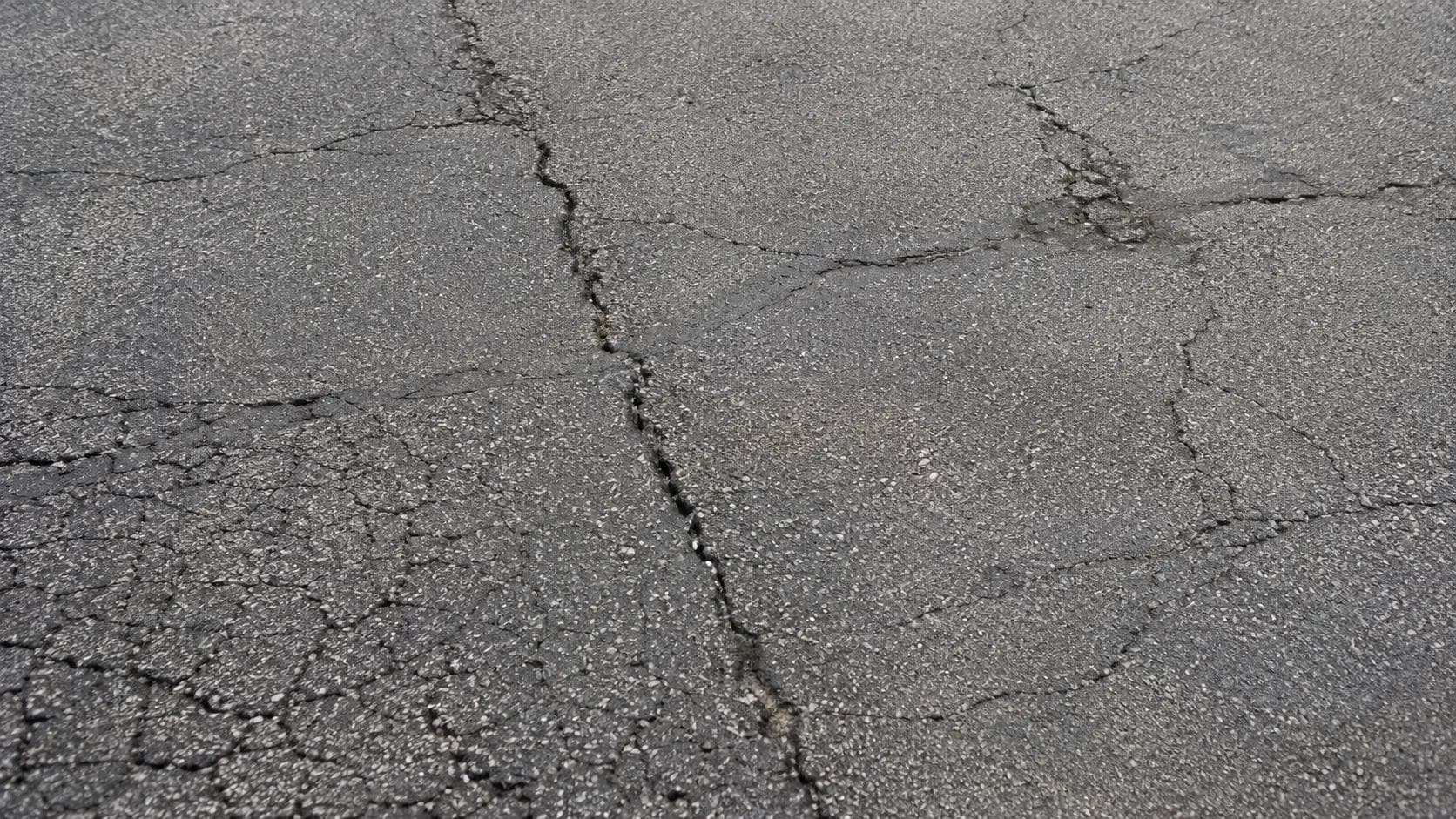 Commercial parking lot surface showing longitudinal cracking and early stage alligator cracking pattern
