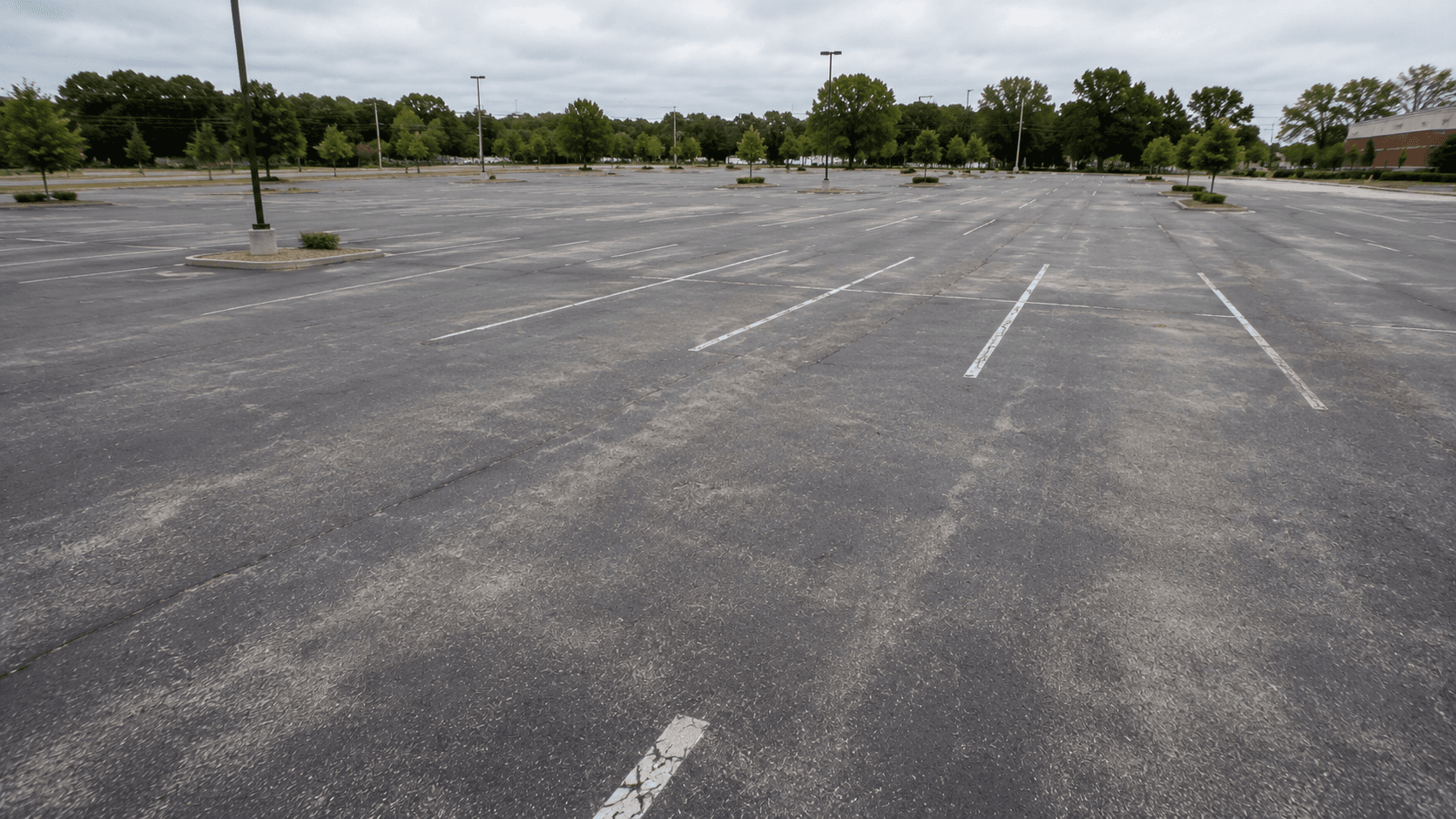 Faded gray oxidized commercial parking lot surface showing early seal coating warning signs