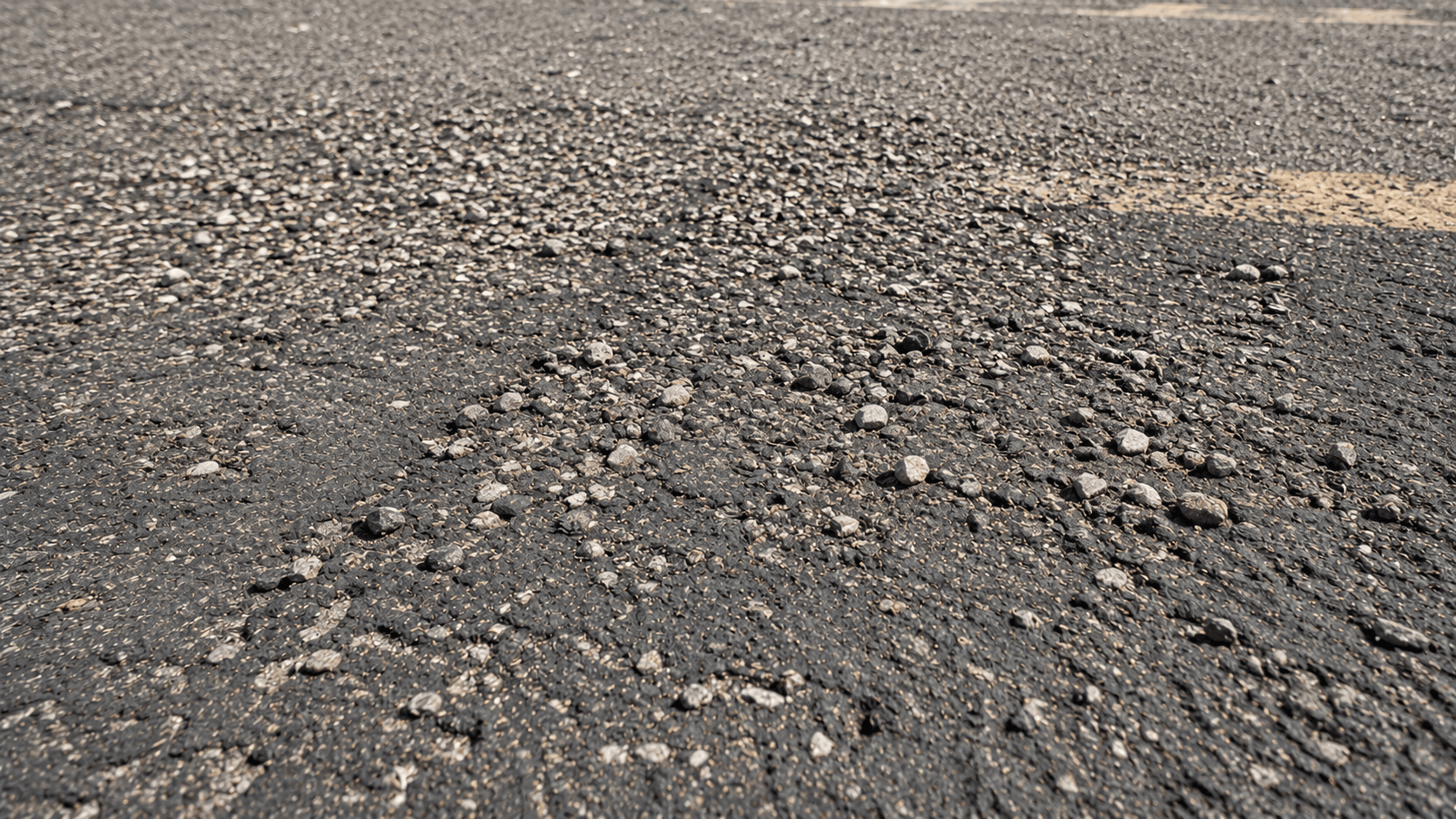 Raveling asphalt surface with loose aggregate from prolonged sun exposure