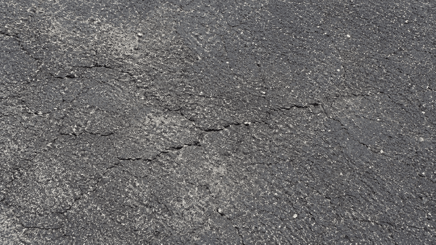Close-up of faded, oxidized asphalt with fine hairline surface cracks before seal coating