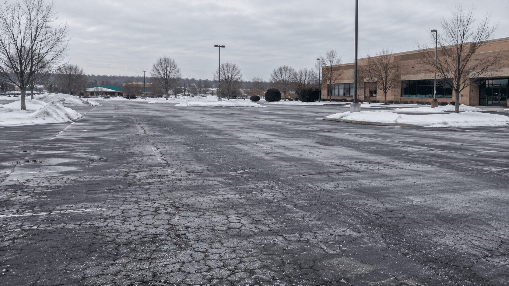 Snow-lined commercial parking lot in the Northeast with cracked, salt-stained asphalt