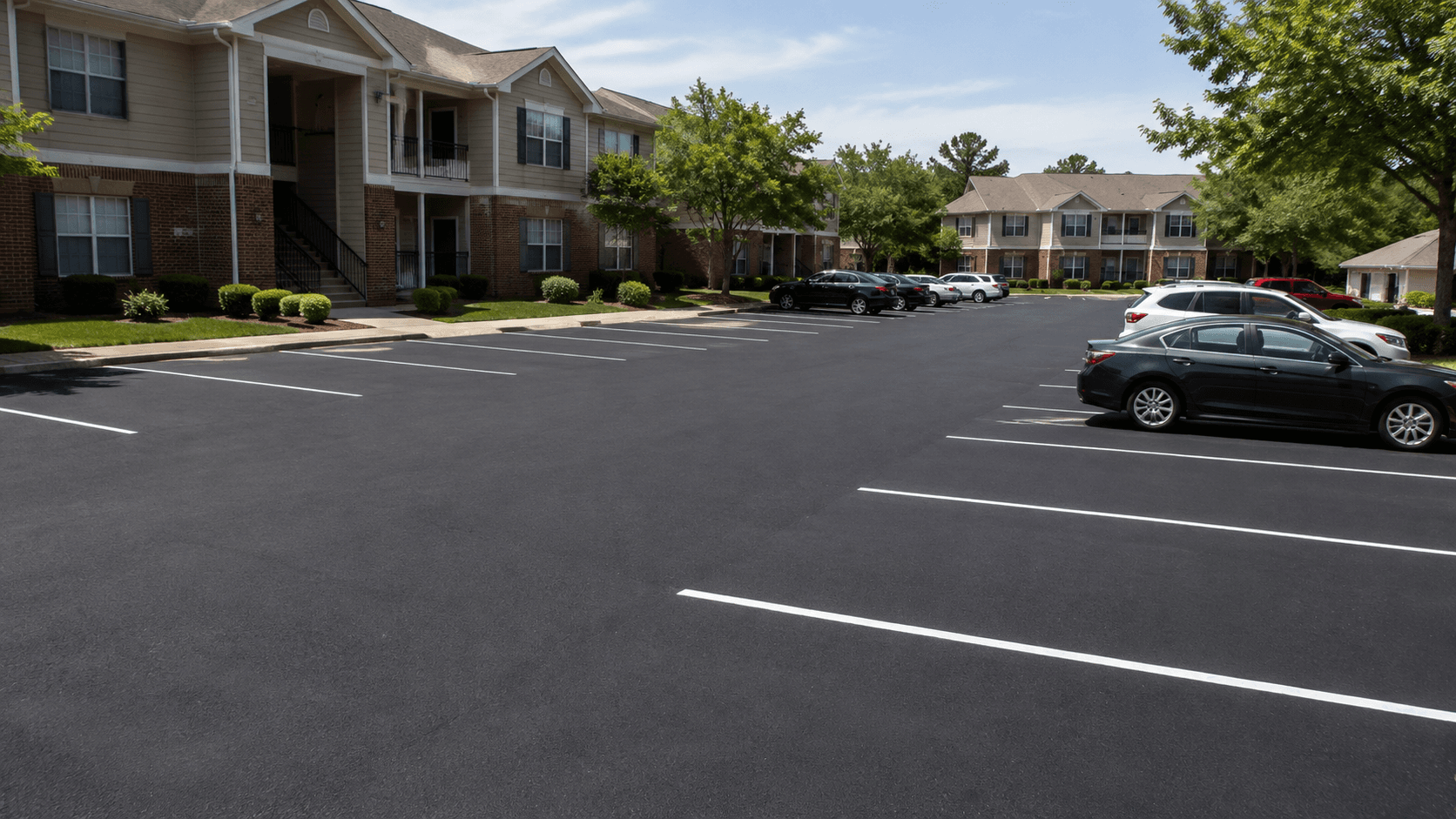 Freshly paved multi-family apartment complex parking lot with resident vehicles nearby